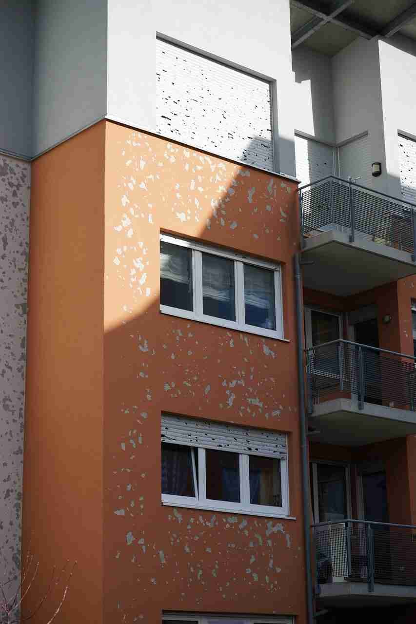All Hail Fiber Cement: How Fiber Cement Siding Protects Homes 3 A multi-story building with orange and white paint peeling, showing three windows and balconies.