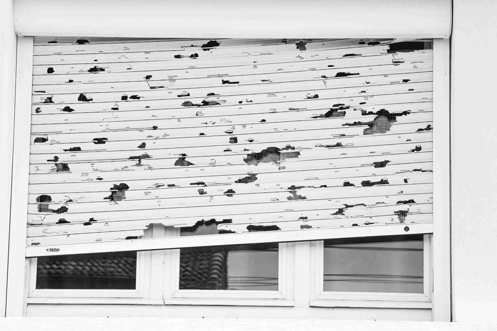 All Hail Fiber Cement: How Fiber Cement Siding Protects Homes 2 Damaged white window shutter with numerous holes and chipped areas above a set of windows.