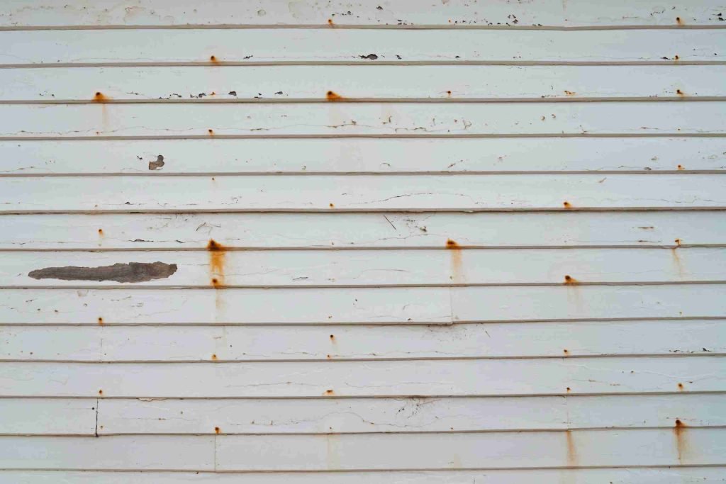 Close-up of a white wooden wall with horizontal panels showing signs of peeling paint, rust, and weathering.