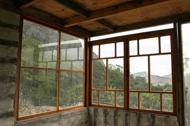 An indoor corner comprised of windows. One is a 4 pane and the other has multiple panes. The frames are made of natural brown wood.