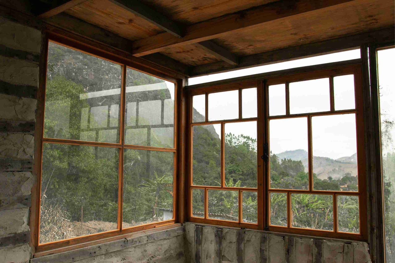 An indoor corner comprised of windows. One is a 4 pane and the other has multiple panes. The frames are made of natural brown wood.