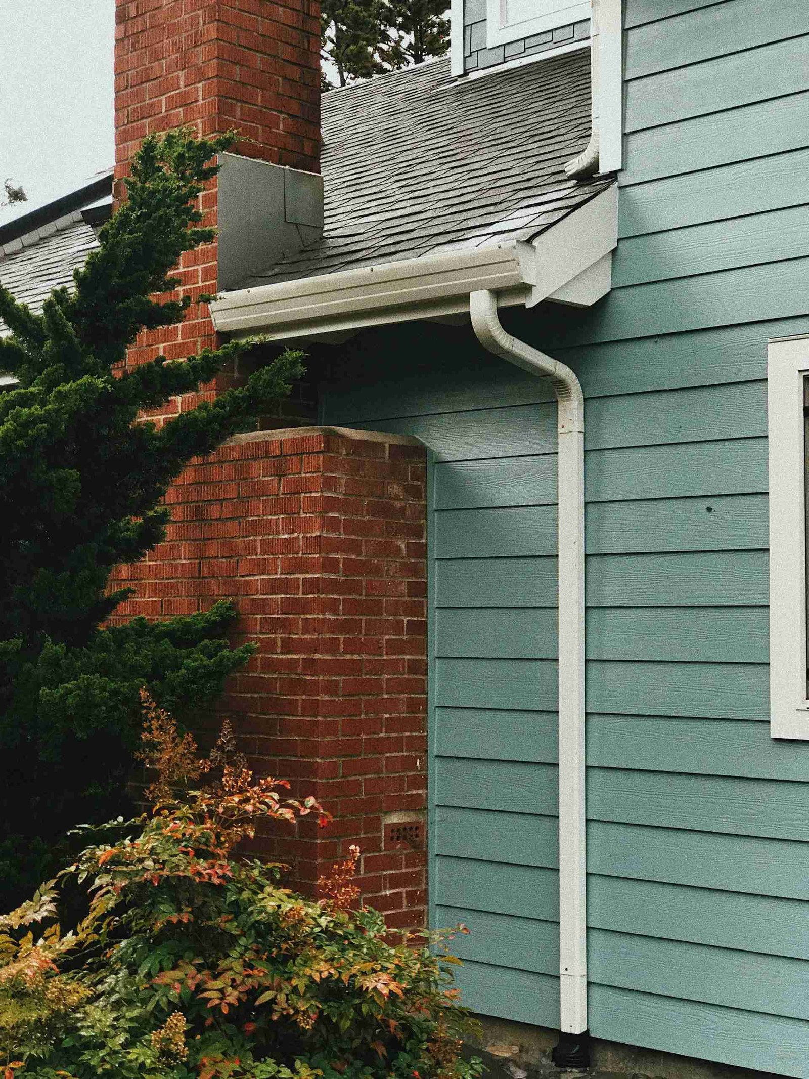 How to Choose the Best Siding for Your Home: Expert Tips and FAQs 2 A house exterior with teal siding and a red brick chimney.